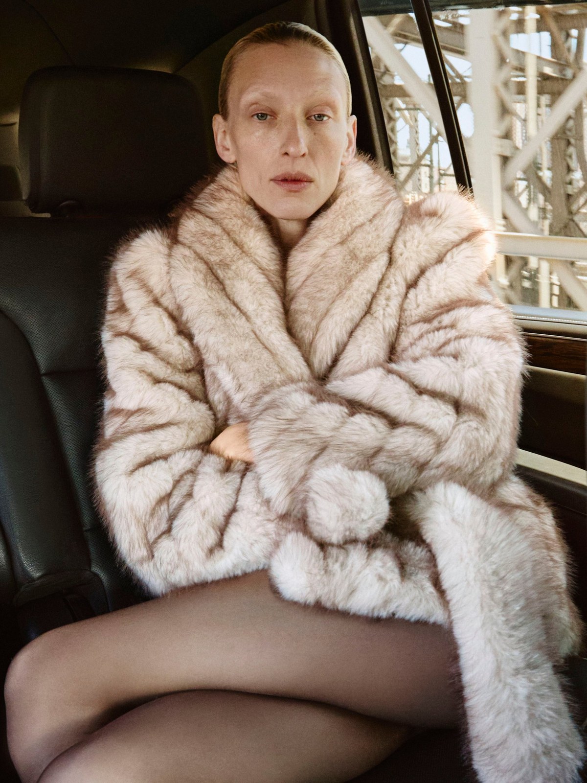 Model seated in a pale faux-fur coat inside a car