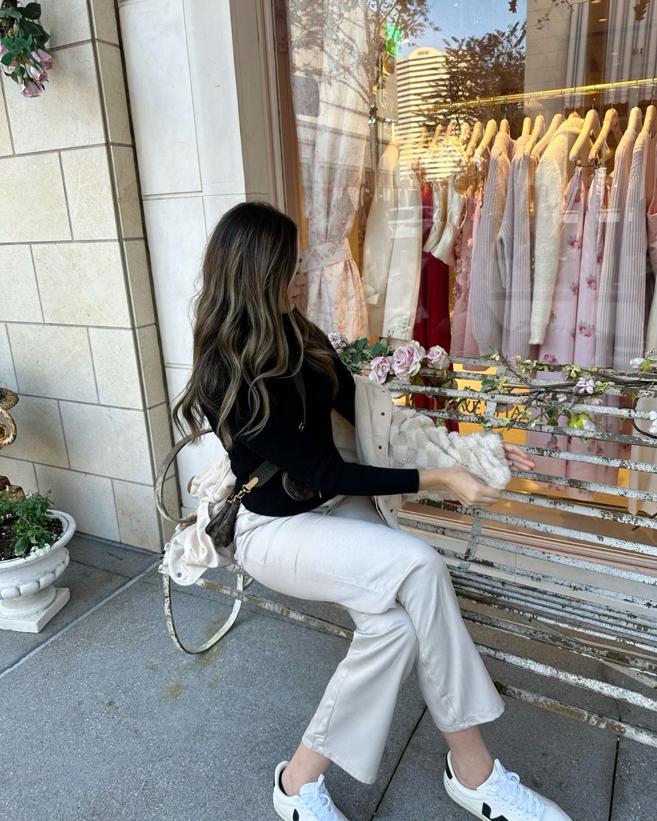 Woman outside a shop in a black top and white jeans wearing white VEJA sneakers