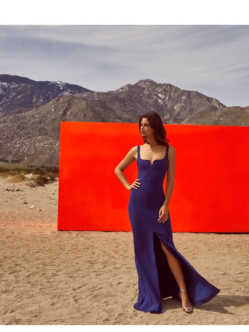 Model in a navy LIKELY gown against a red wall in a desert landscape