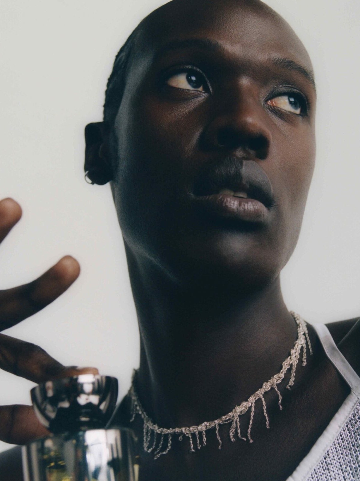 Model wearing a dark sleeveless top with fragrance in hand