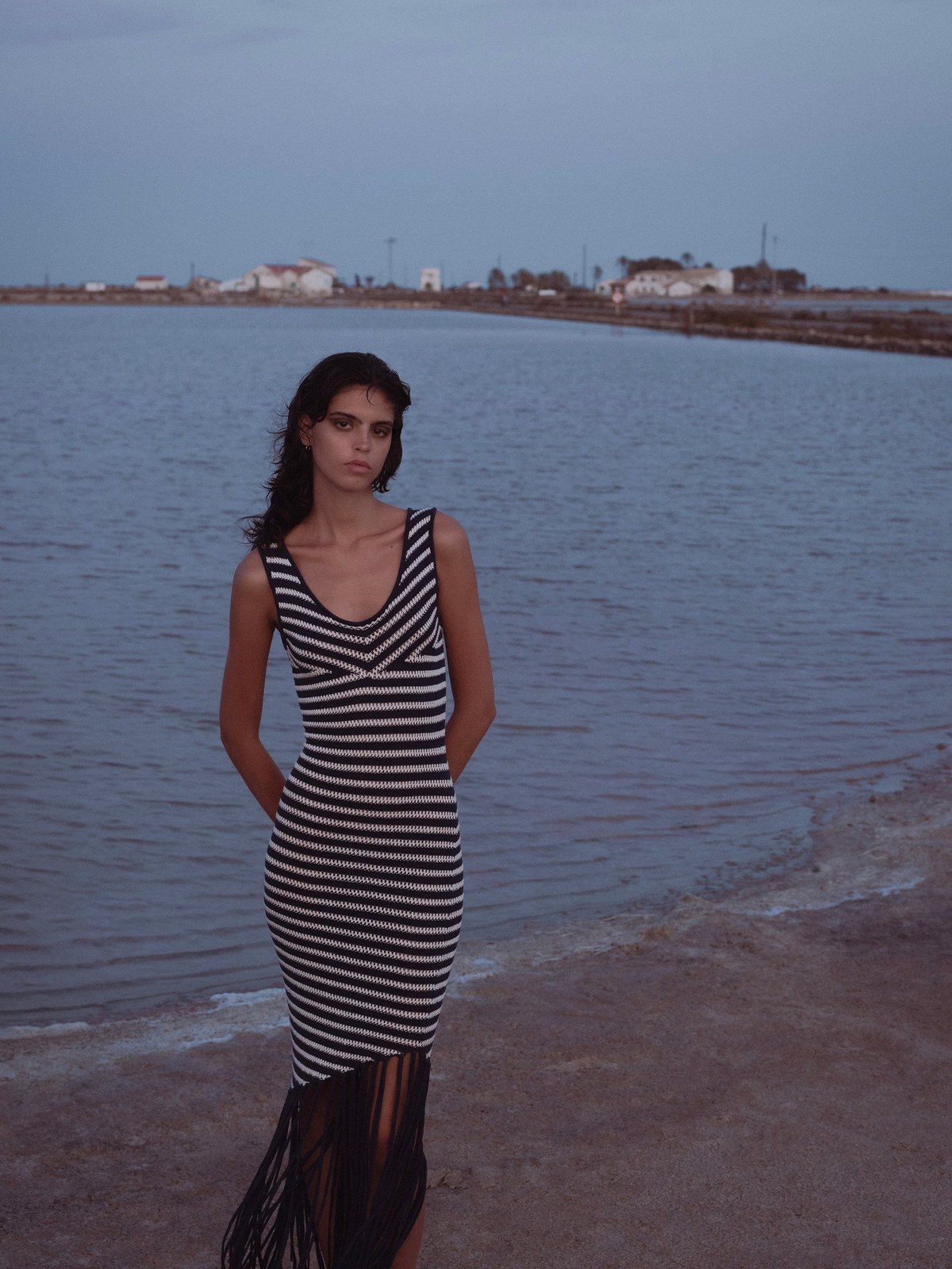 Model wearing a striped sleeveless dress beside calm water