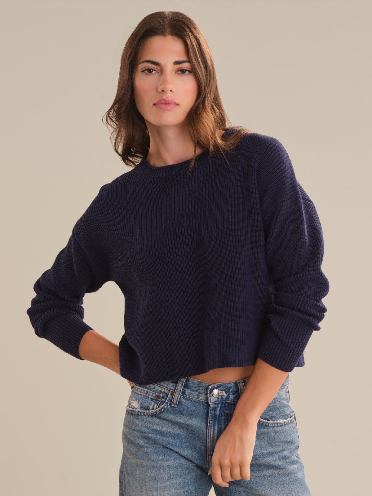 Model in a navy sweater and denim against a warm studio backdrop
