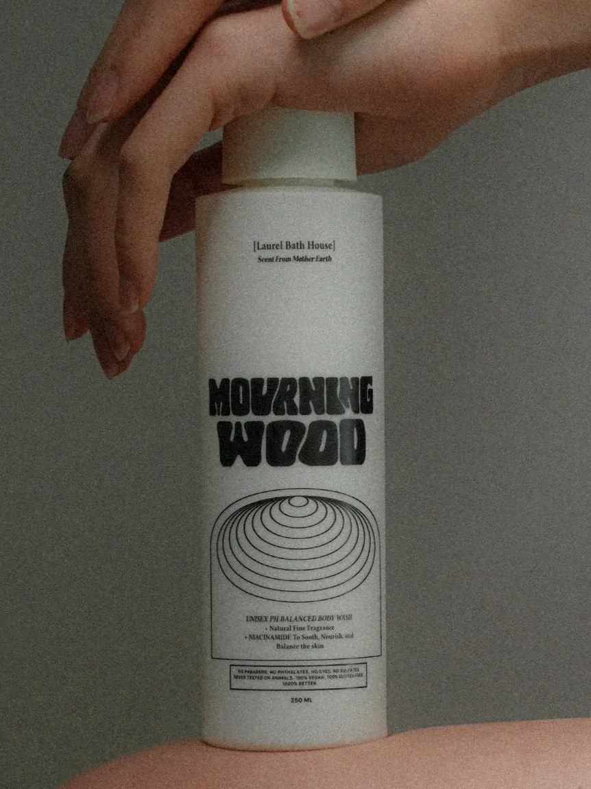 Hands and bare skin around a Laurel Bath House body wash bottle in a softly lit campaign image