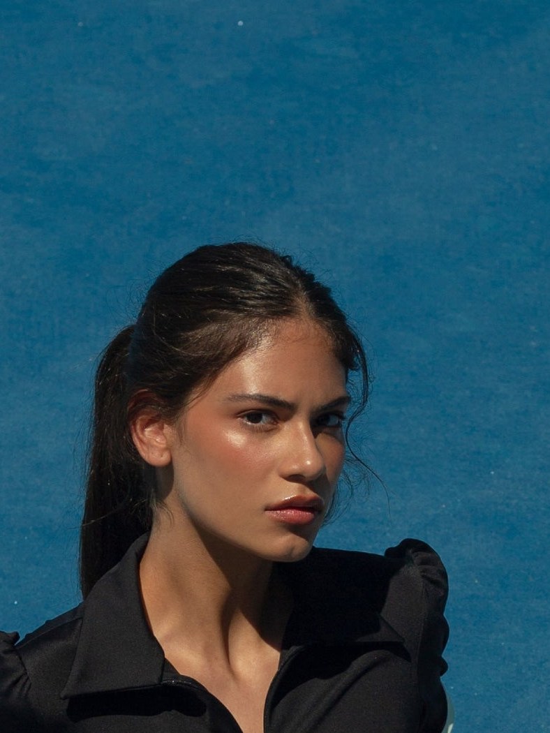 Close portrait of a model in a black zip-neck dress against a blue court
