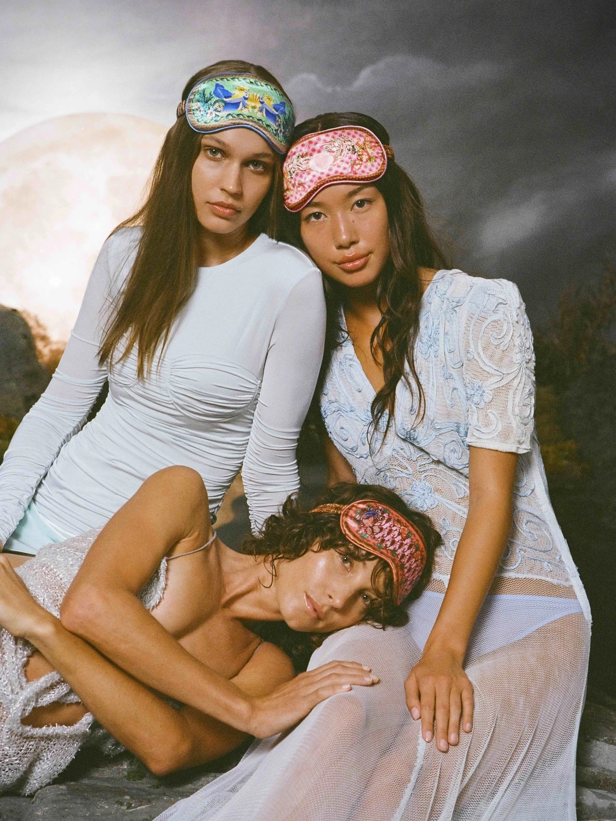 Models in silk sleep masks reclining together in a styled setting