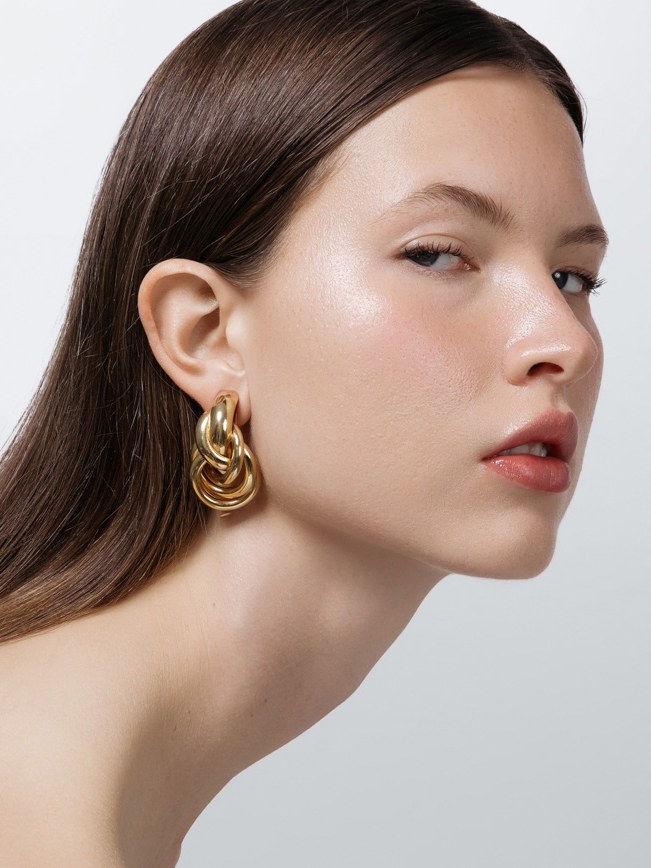 Model in profile wearing sculptural SHASHI gold-tone earrings