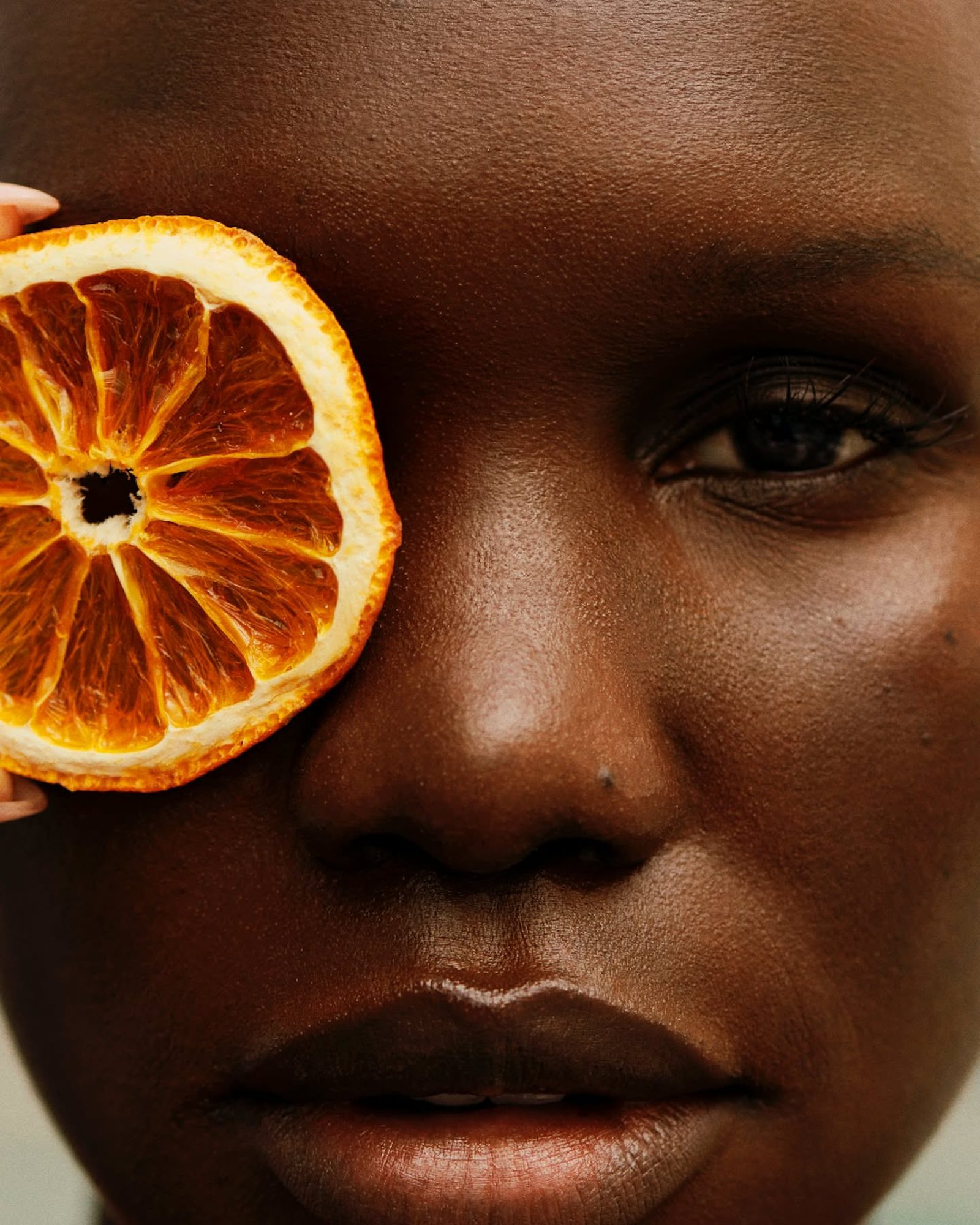 Close-up of a woman's face with a dried orange slice held over one eye