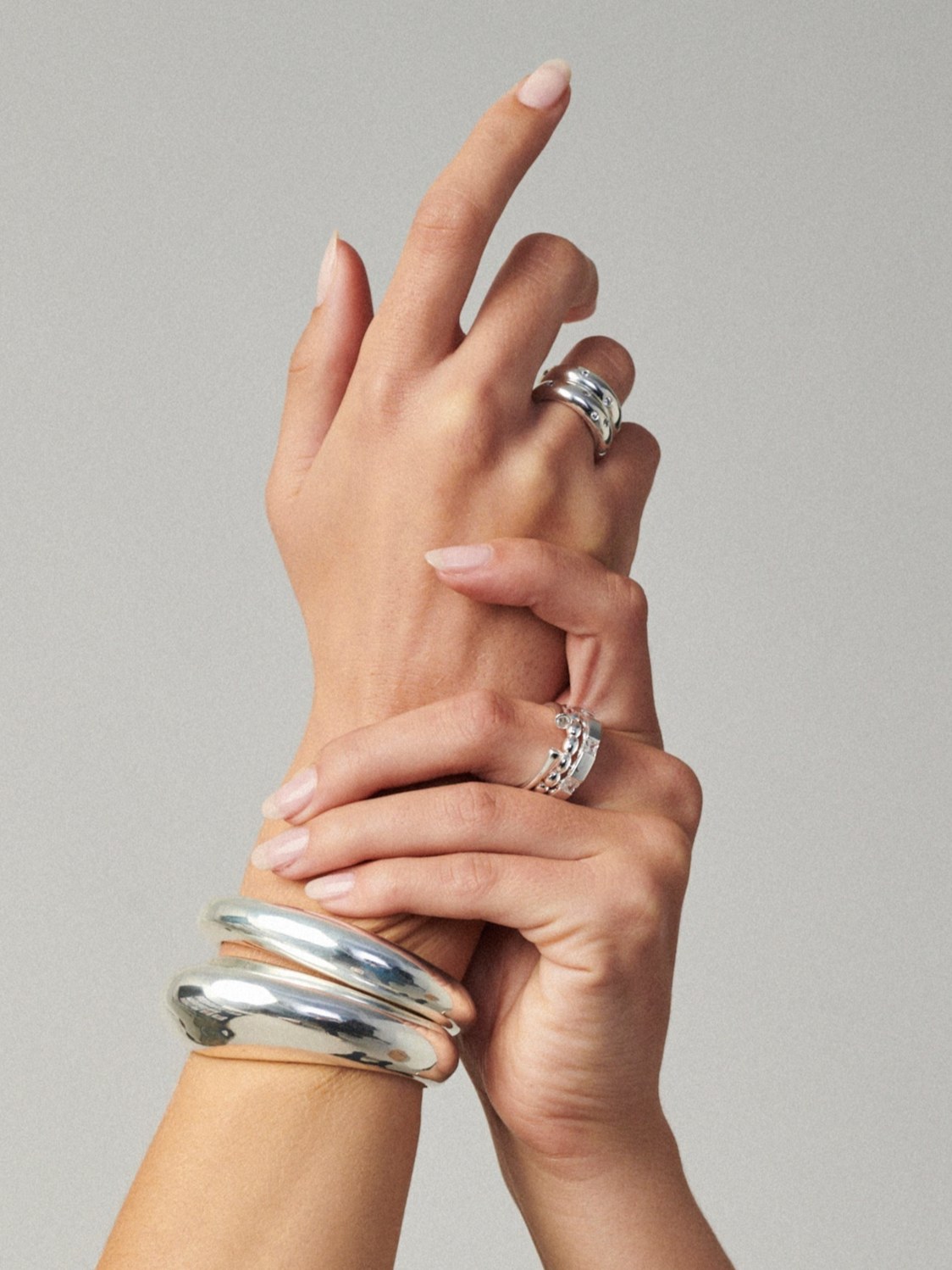 Hands wearing sculptural silver bracelets and rings