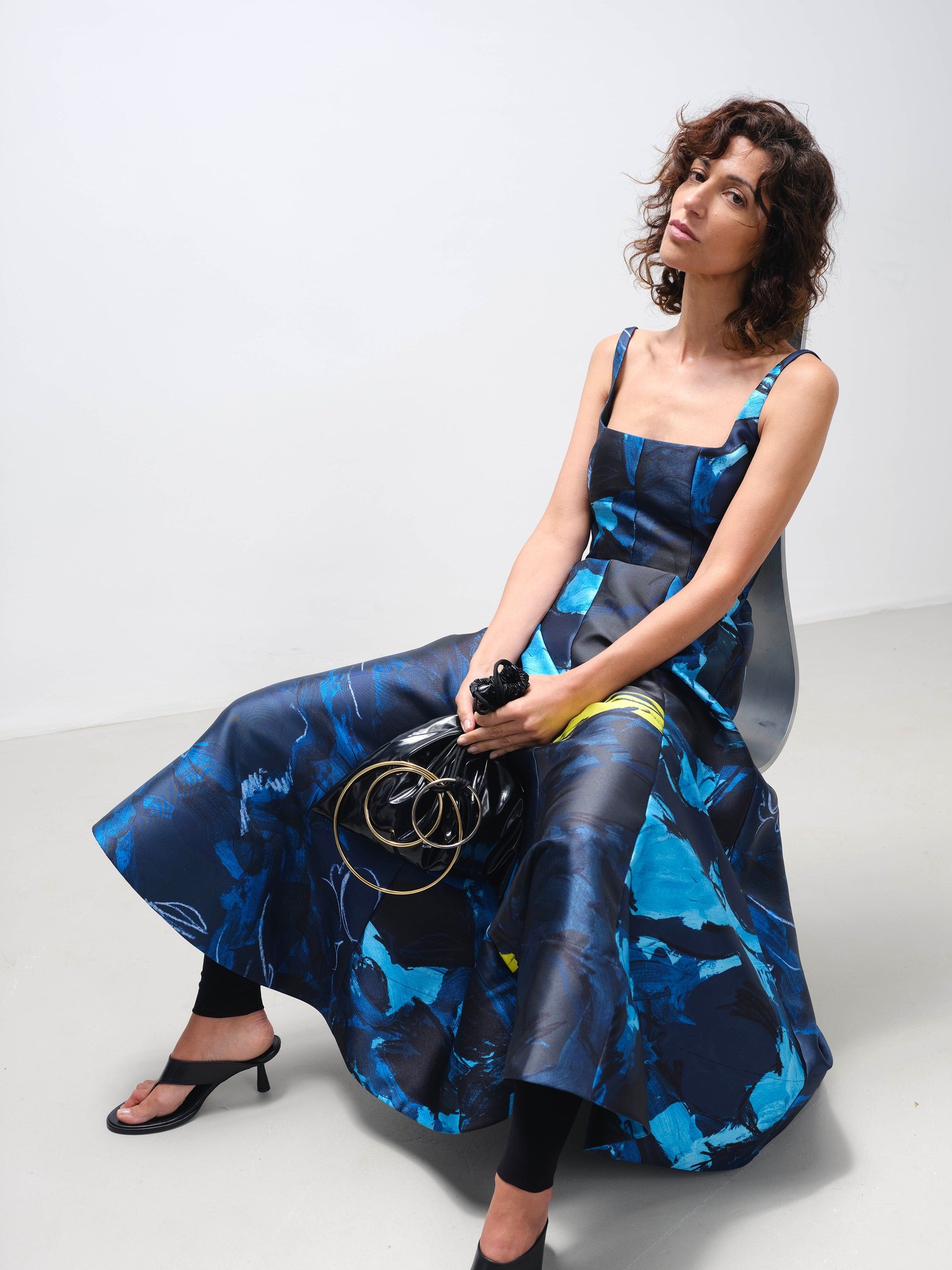 Seated model in a blue and teal printed square neck dress with sandals