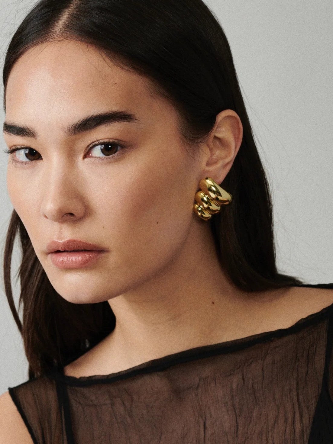 Model wearing large gold earrings in a sheer black top