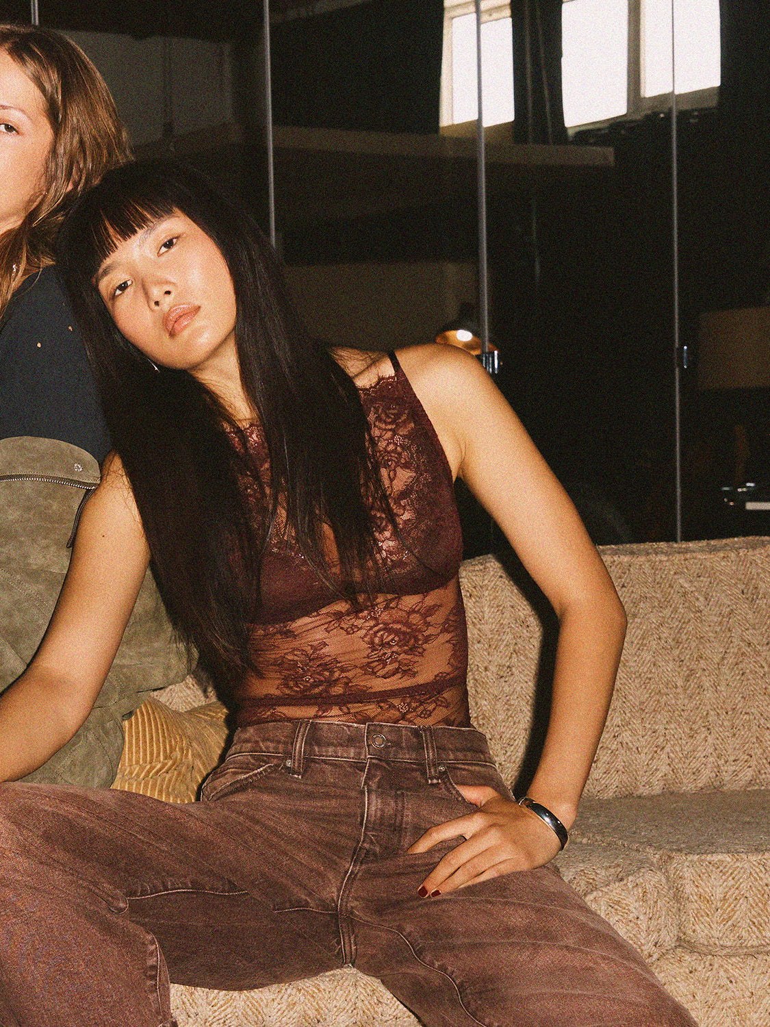 Model in a burgundy lace top and brown jeans on a living room sofa