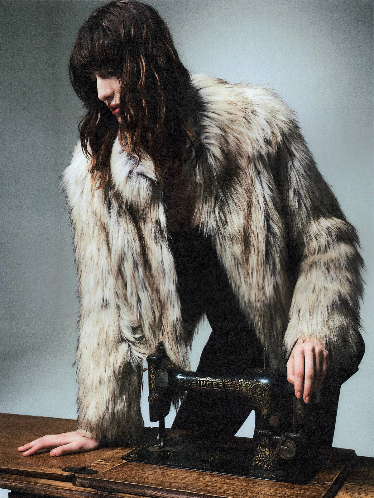 Model in a pale faux fur coat beside a vintage sewing machine