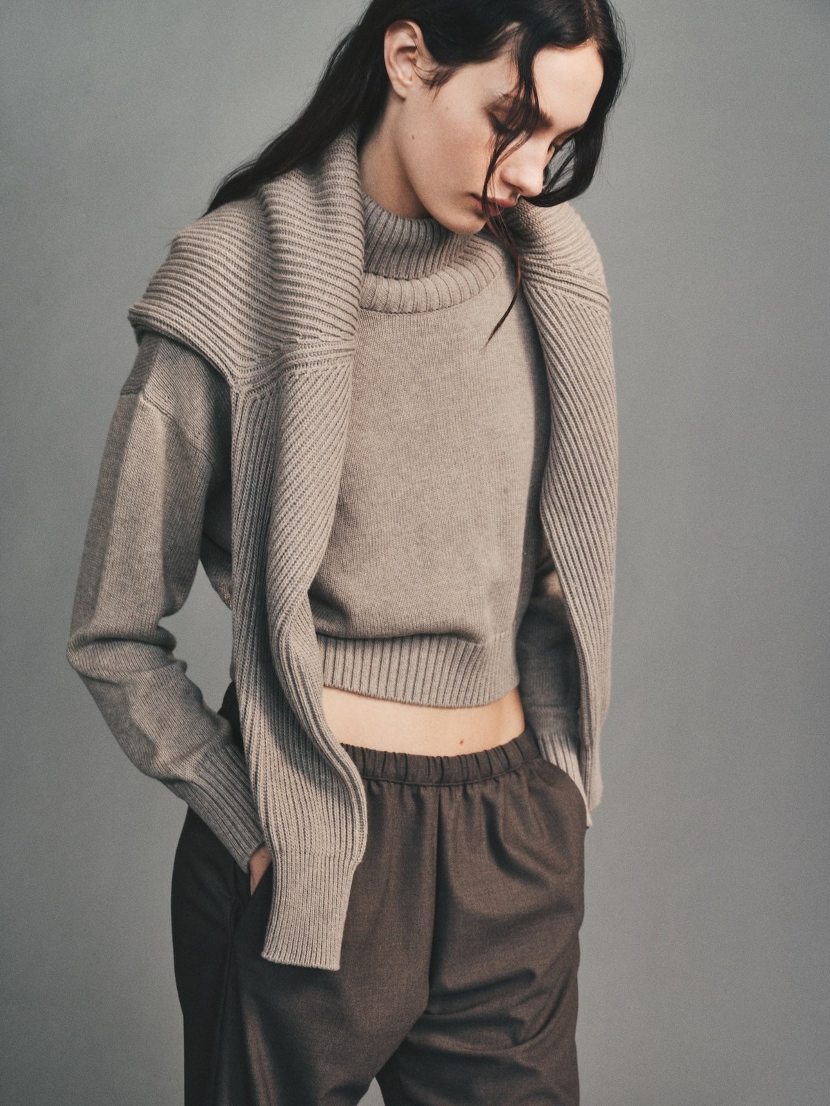 Model in a taupe knit top and draped scarf with dark trousers