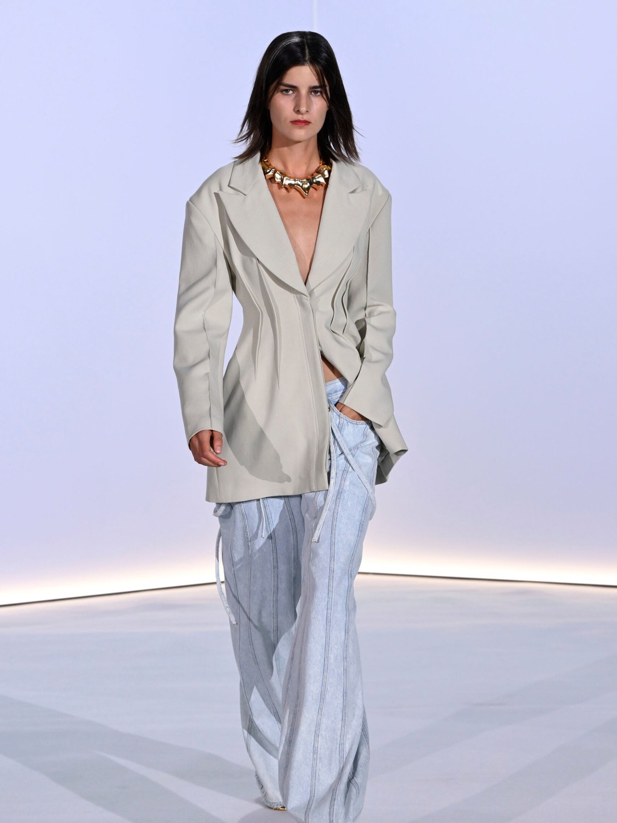 Model in a pale tailored look and gold jewelry on the runway