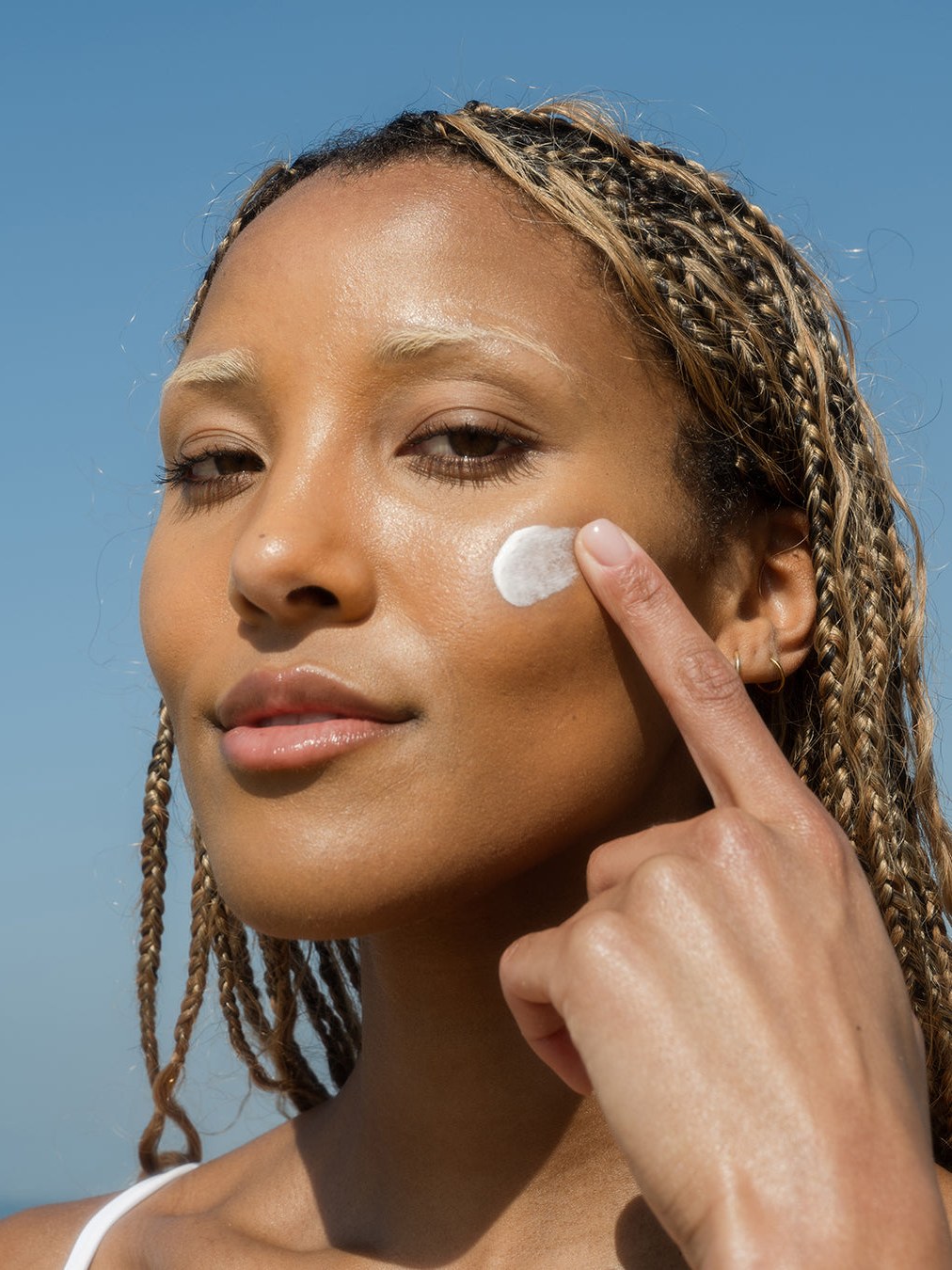 Woman applying face sunscreen to her cheek in bright coastal light